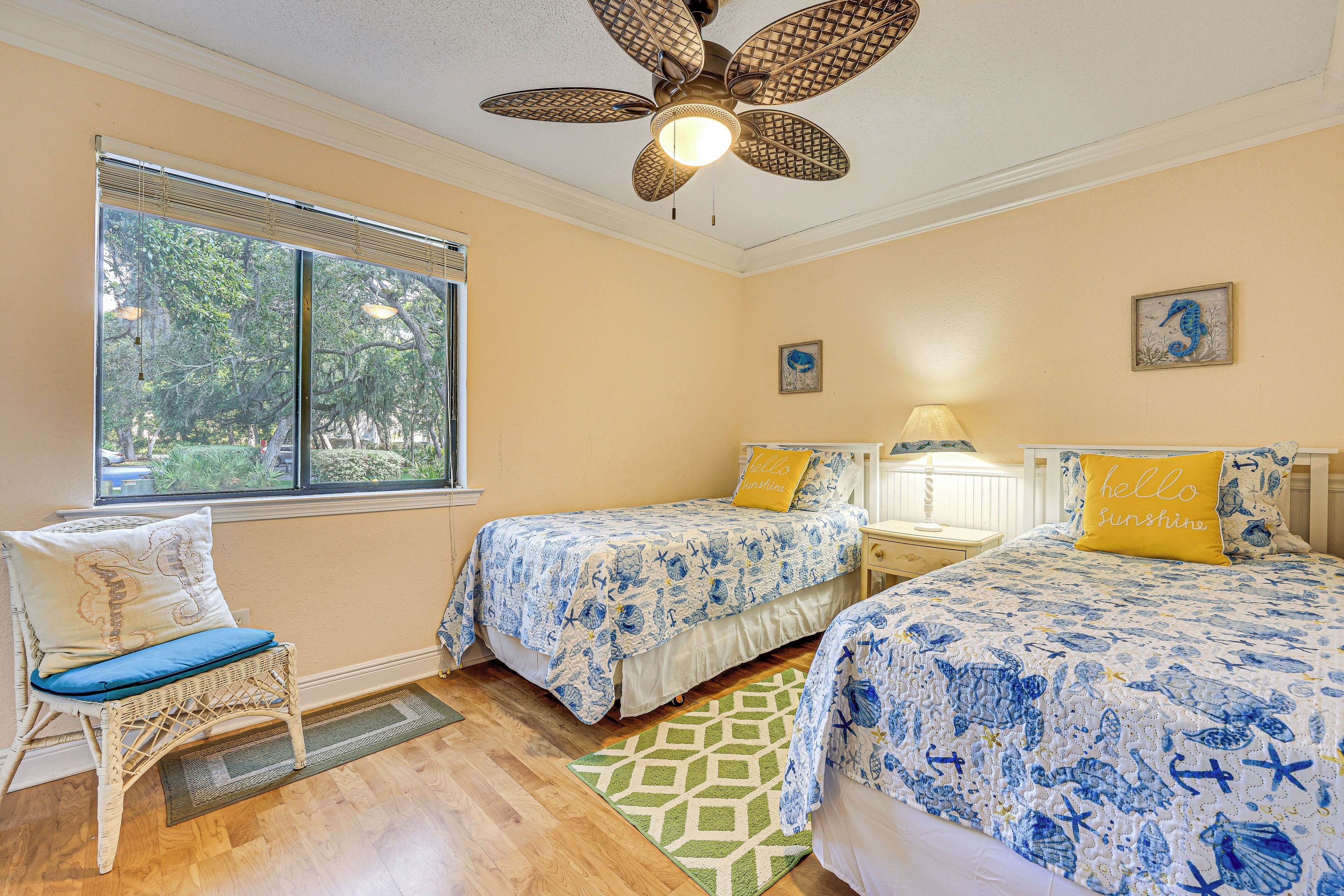 A bedroom with two beds, a chair, a ceiling fan, and a window with blinds.