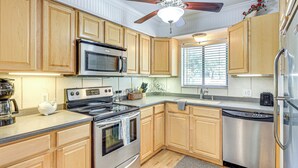 A kitchen with wooden cabinets, stainless steel appliances, a ceiling fan, and a window with blinds. - Fernandina Beach Condo w/ Pool + Path to Beach! (Fernandina Beach)