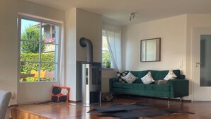 Un salon moderne avec un canapé vert, une cheminée, un plancher en bois et de grandes fenêtres.