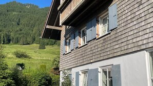 Une maison en bois avec un balcon, un banc en bois et un chemin de pierre menant à l’entrée.