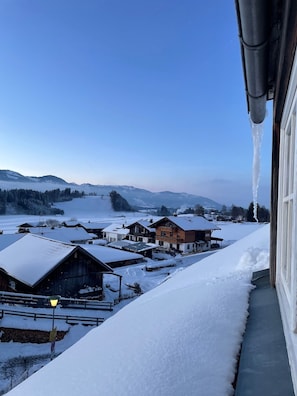 Ein verschneites Dorf mit Häusern, einem klaren Himmel und Blick auf ferne Berge.
