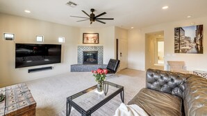 A living room with a flat-screen TV, a fireplace, a ceiling fan, and a large couch. - Phoenix Condo ~ 1 Mi to Desert Ridge Marketplace! (Phoenix)