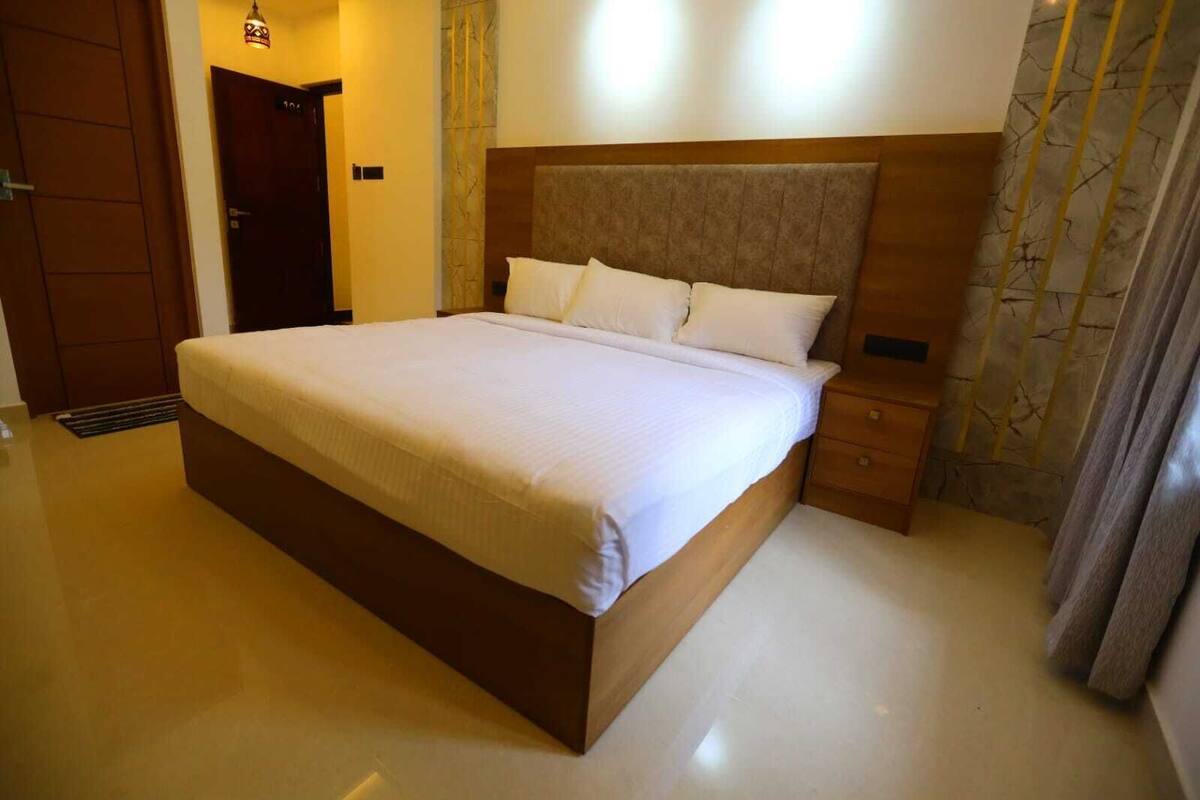 Una habitación de hotel con una cama grande, un cabecero de madera, una mesita de noche y una puerta.