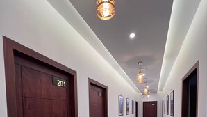 Un couloir d’hôtel avec des portes en bois numérotées 201 et 204, un plancher ciré et des luminaires suspendus.