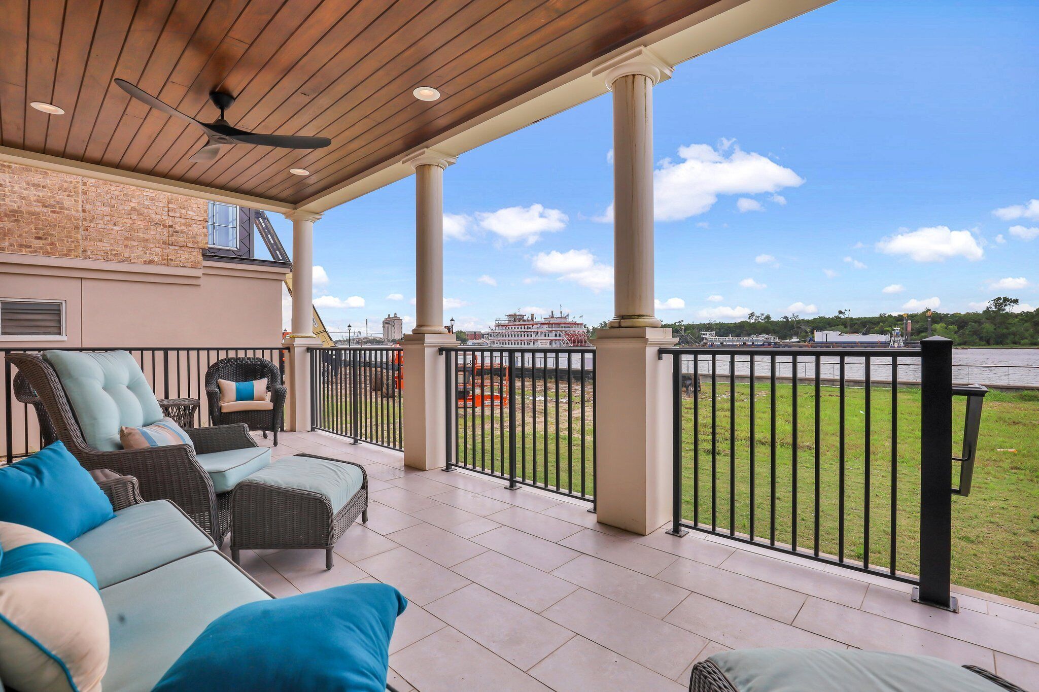 Une terrasse couverte, meublée de mobilier en osier, avec vue sur une rivière et un mur en briques.
