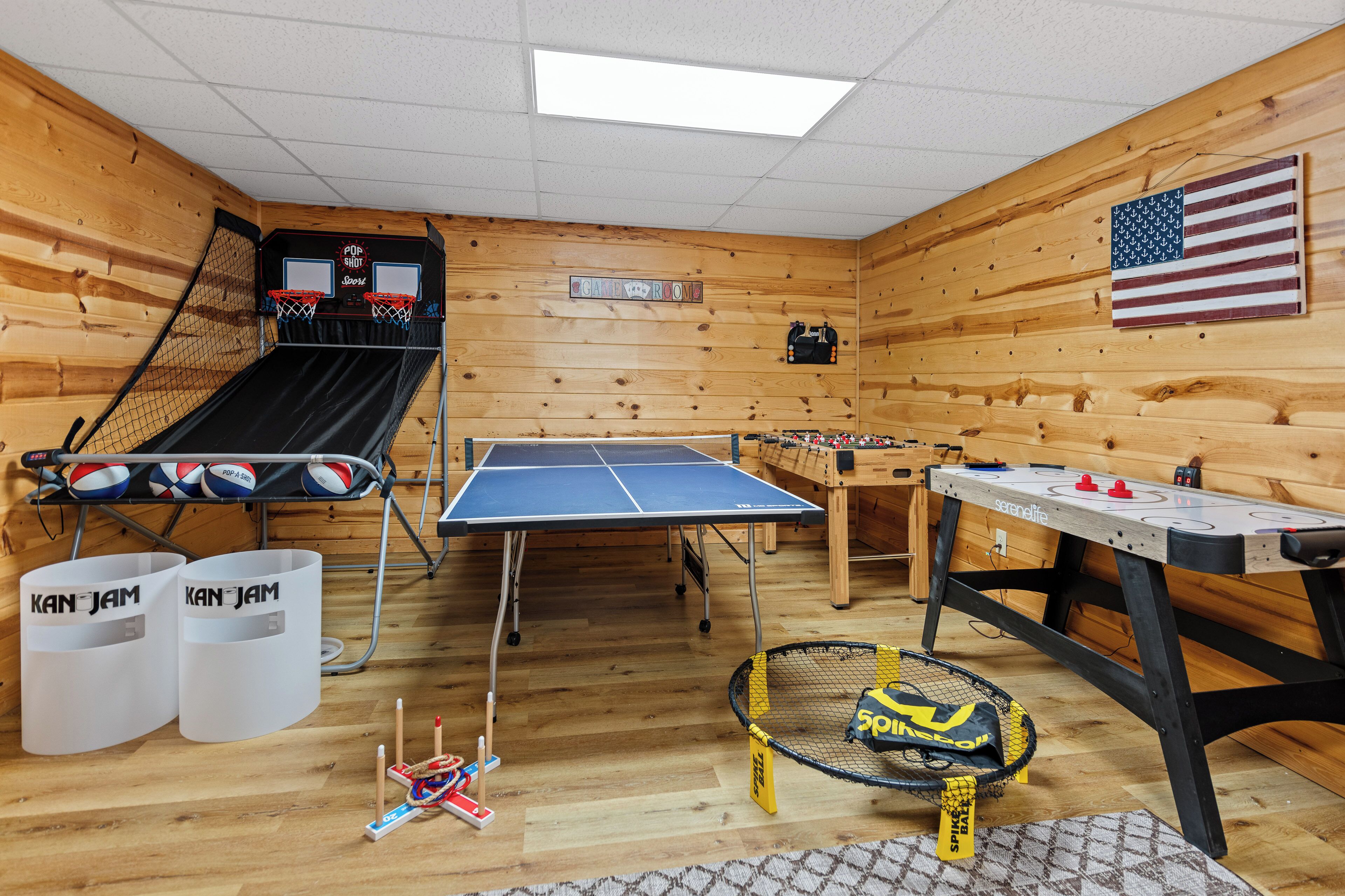 A recreational room with a ping pong table, foosball table, and a basketball hoop.