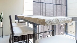 Un balcón con un borde de piedra, sillas de mimbre con cojines y una planta en maceta.