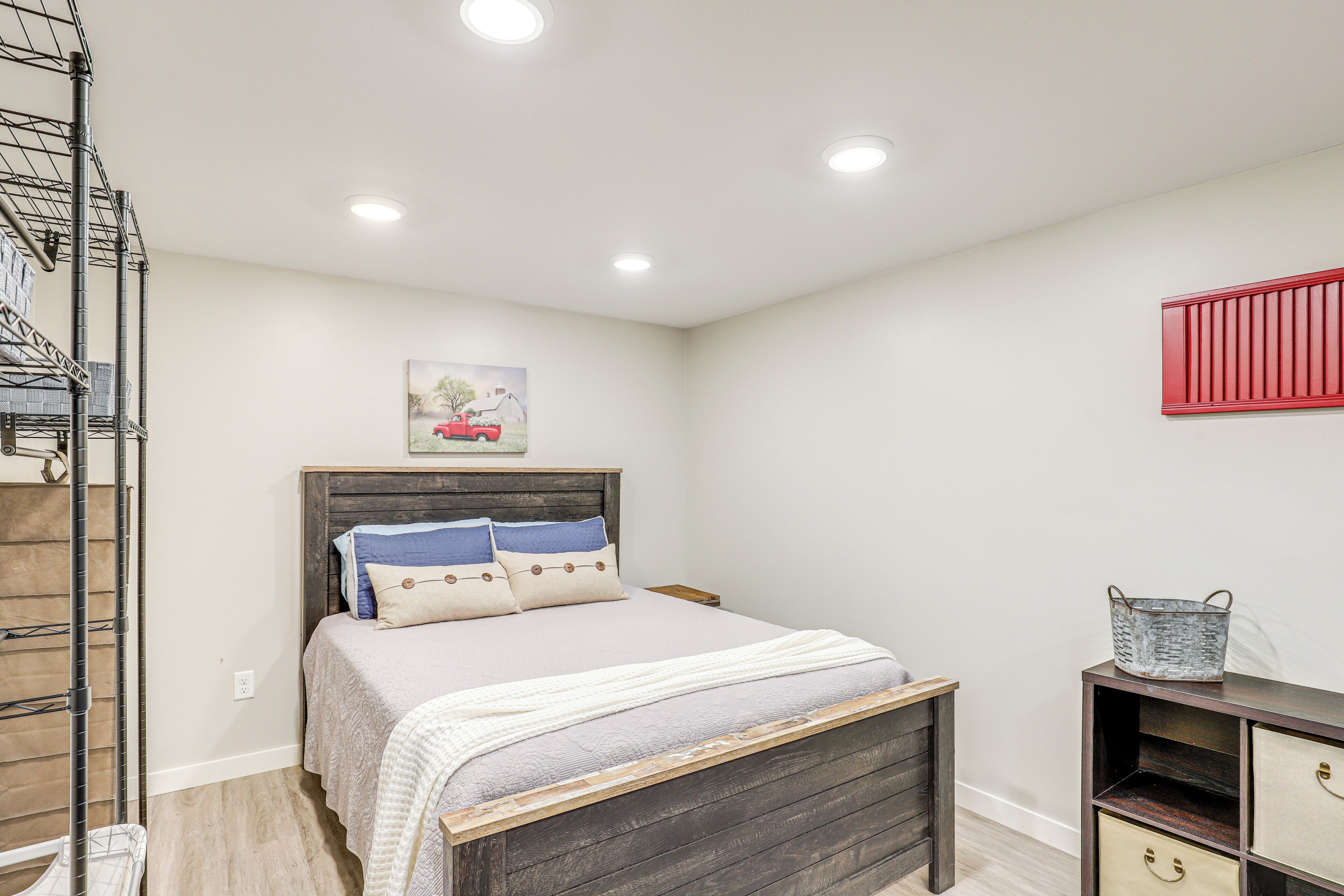 A bedroom with a wooden bed, a nightstand, a red shelf, and a wall-mounted shelf.