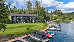 A multi-story building with balconies, a grassy area, and a dock with boats. - Waterfront Condo 5-Minute Walk to DT Bigfork (Bigfork)
