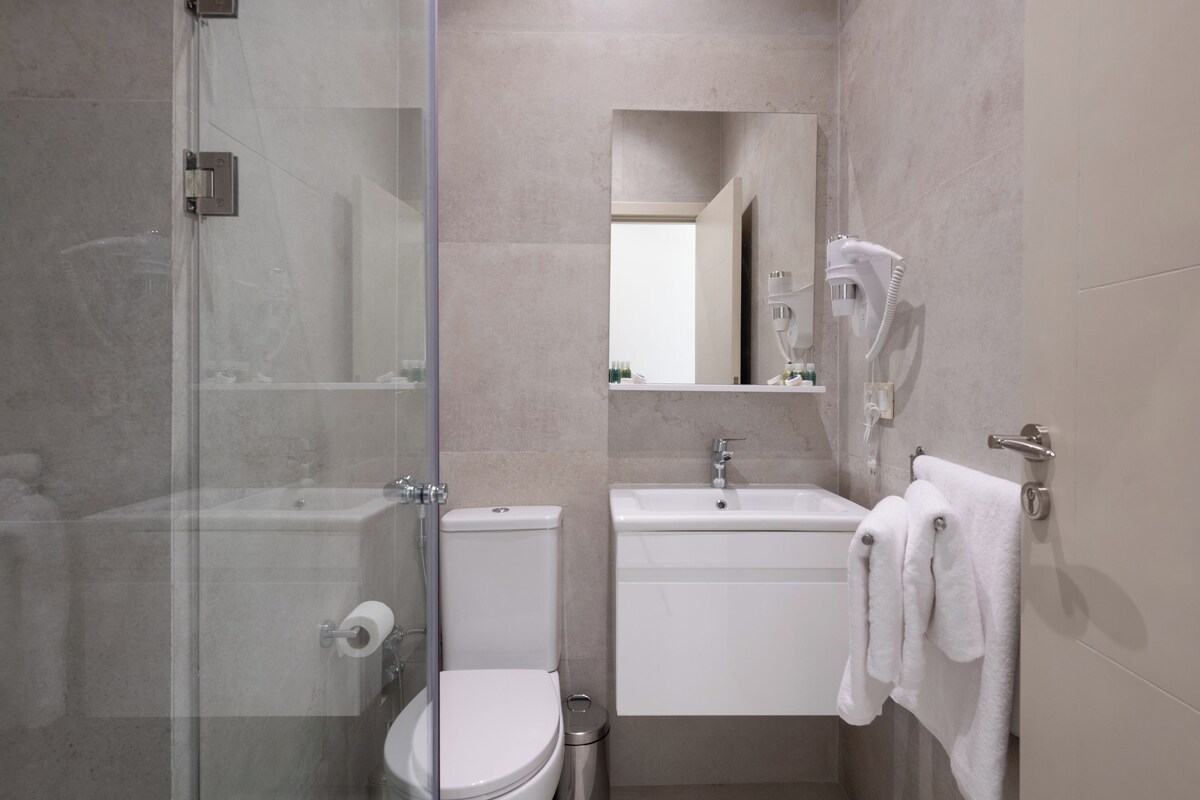 Ein modernes Badezimmer mit Glasdusche, Toilette, Waschbecken und Handtuchhalter.