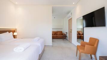 Une chambre d’hôtel avec un grand lit, une chaise, un téléviseur fixé au mur et un canapé à l’arrière-plan.