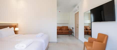 A hotel room with a large bed, a chair, a TV mounted on the wall, and a sofa in the background.