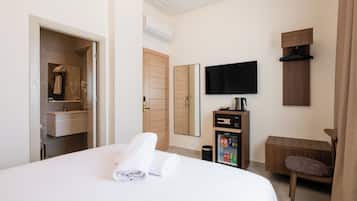 Habitación de hotel con cama, televisión, mini bar, espejo y puerta que da a un baño.