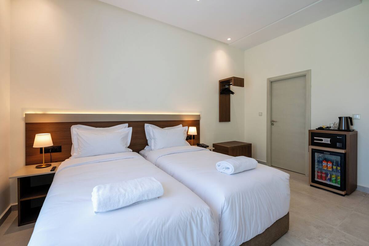 A hotel room with two beds, bedside lamps, a minibar, and a door.
