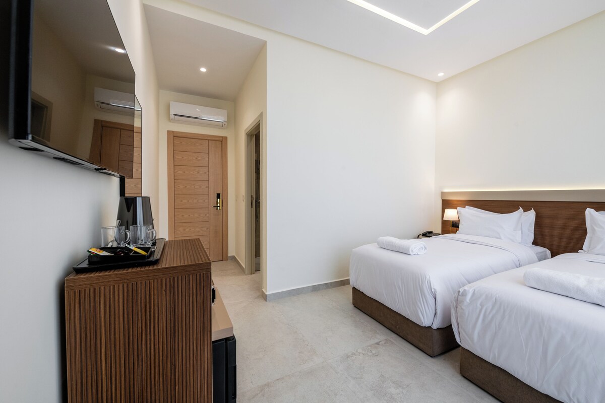 A hotel room with two beds, a wooden desk, a flat-screen TV, and a mirror.