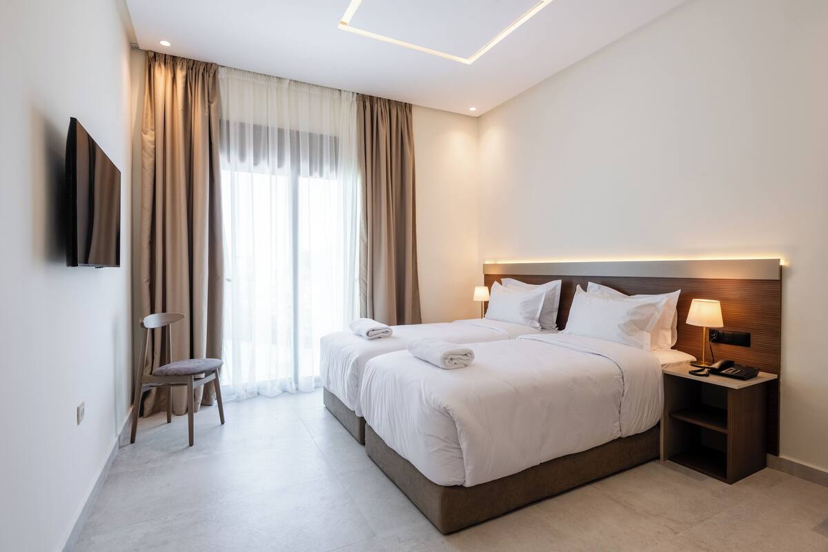 A modern hotel room with a large bed, bedside tables, a flat-screen TV, and a window with curtains.