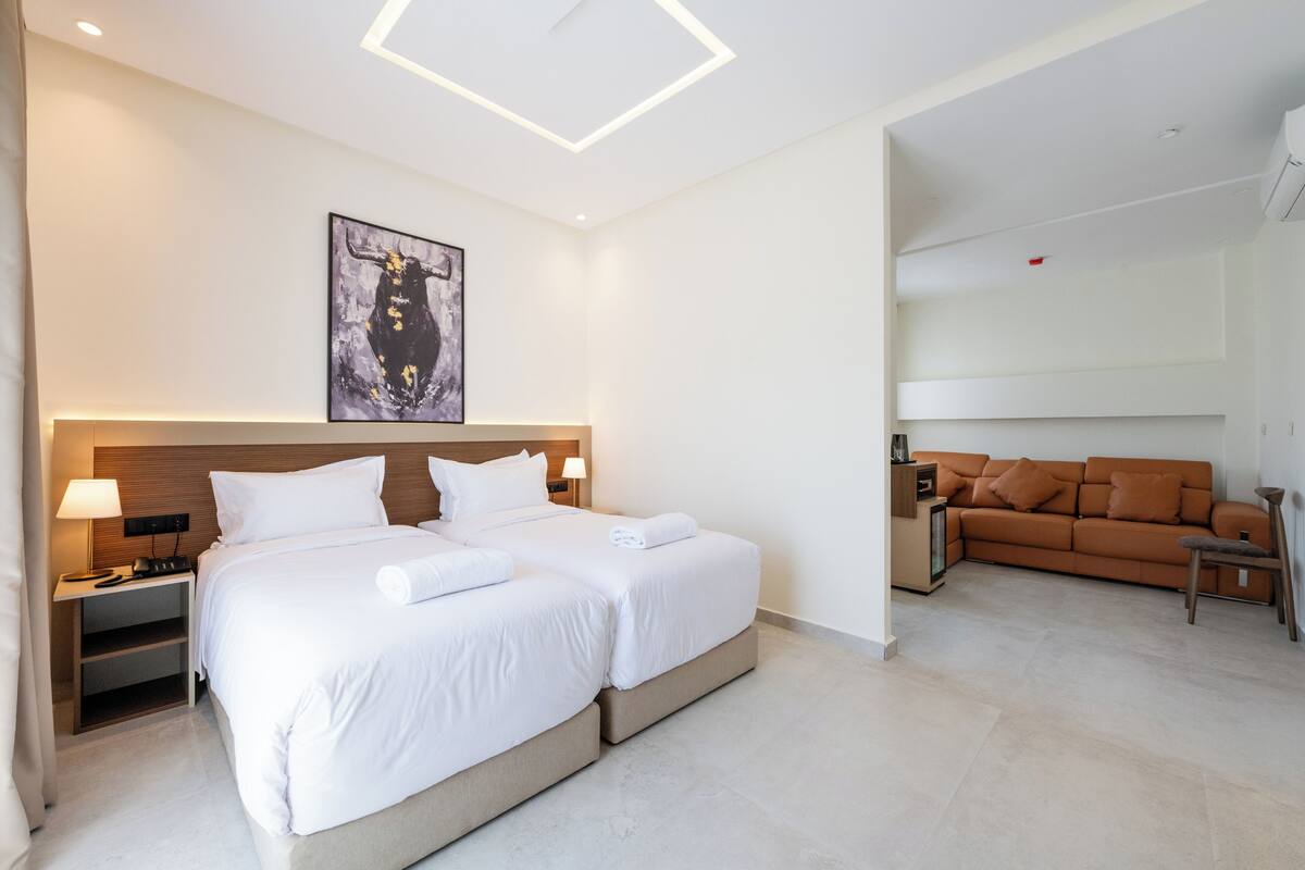 A modern hotel room with a large bed, a sofa, and a painting on the wall.