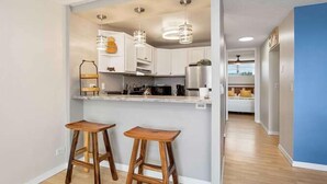 Una cocina moderna con armarios blancos, dos taburetes de madera y luces colgantes.
