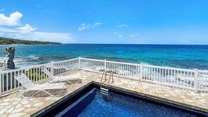 A pool area with a view of the ocean, white railings, and lounge chairs. - Hale Lani:Direct Oceanfront Massive Pool, Gated, Remodeled Beauty (KAILUA KONA)