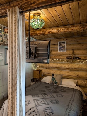 Un dormitorio acogedor tipo cabaña con una cama, un sillón colgante, una mesita de noche de madera y un estante en la pared.