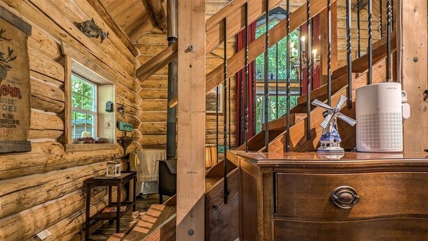 A wooden cabin interior with a staircase, wooden walls, a metal railing, and a dresser with drawers.