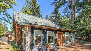 A rustic cabin with a metal roof, wooden logs, and a porch with potted plants.