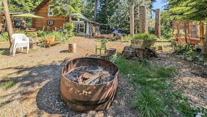 A rustic cabin with a fire pit, outdoor seating, and a forested backdrop.