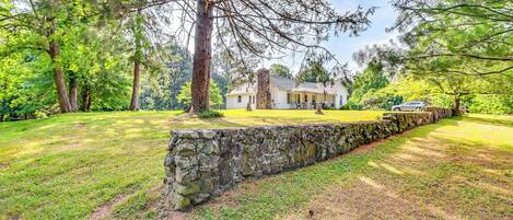 Una casa rodeada por un muro de piedra y abundante vegetación.