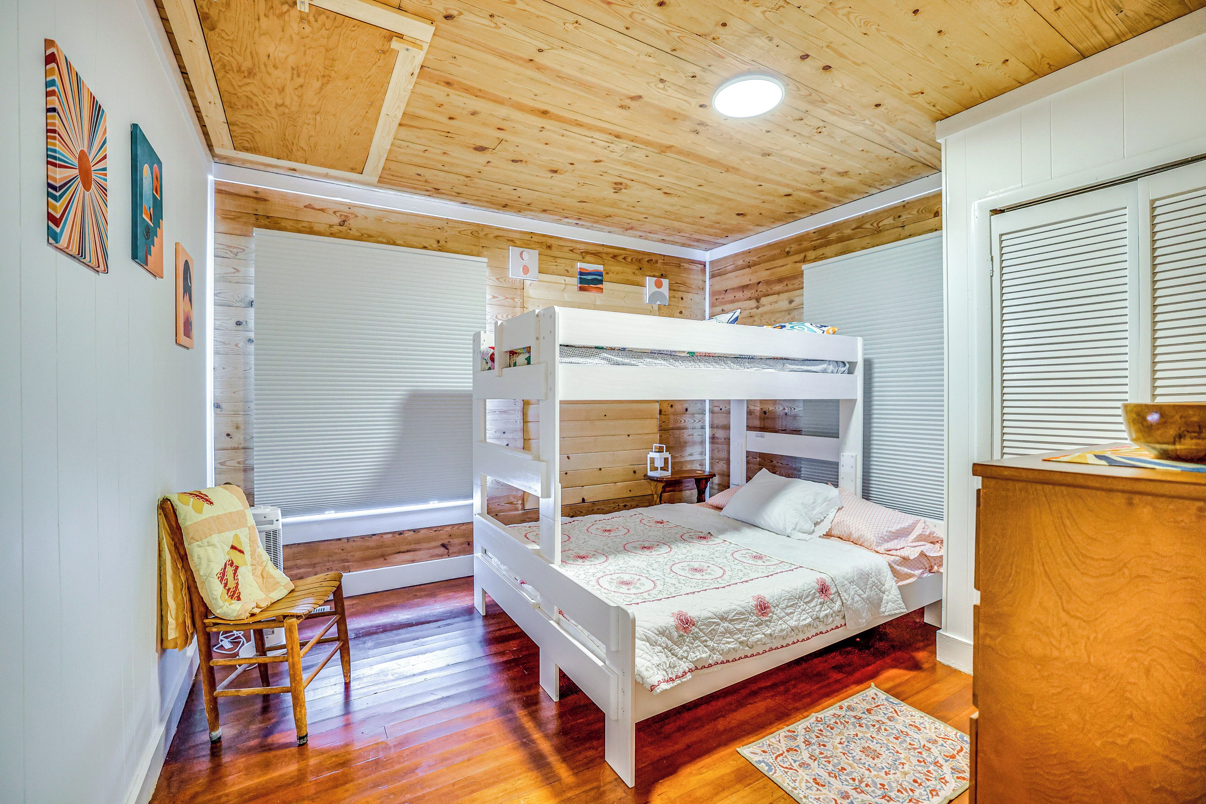 A bunk bed room with wooden walls and a ceiling, a wooden chair, and a small table with a lamp.