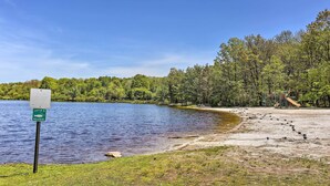 A lakeside area with a catch and release sign, a sandy beach, and a playground structure. - Private Hot Tub: Tree-lined Poconos Home! (Pocono Summit)