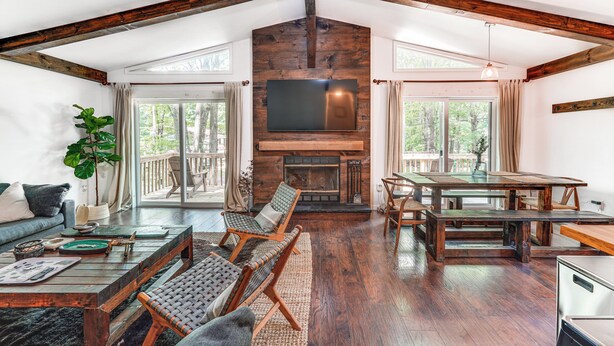 A spacious living area with a fireplace, wooden beams, a large TV, and a dining table. - Private Hot Tub: Tree-lined Poconos Home! (Pocono Summit)