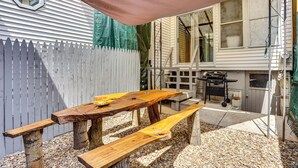 Una mesa de picnic de madera con bancos, una parrilla y una valla de piquetes blancos en un patio trasero.