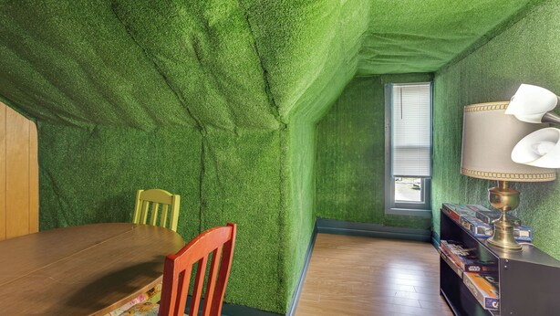 Una habitación con pared verde con textura, una mesa de comedor de madera, una silla roja, una estantería con libros y una lámpara.
