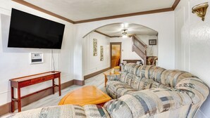 Una sala de estar con un televisor de pantalla plana grande, una mesa de centro de madera y un sofá estampado.