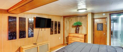A hotel room with wooden paneling, a bed, a television, artwork on the wall, and a sign on the door.
