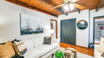 A living room with a white sofa, a ceiling fan, a painting of a sailboat, a door, and a mirror.
