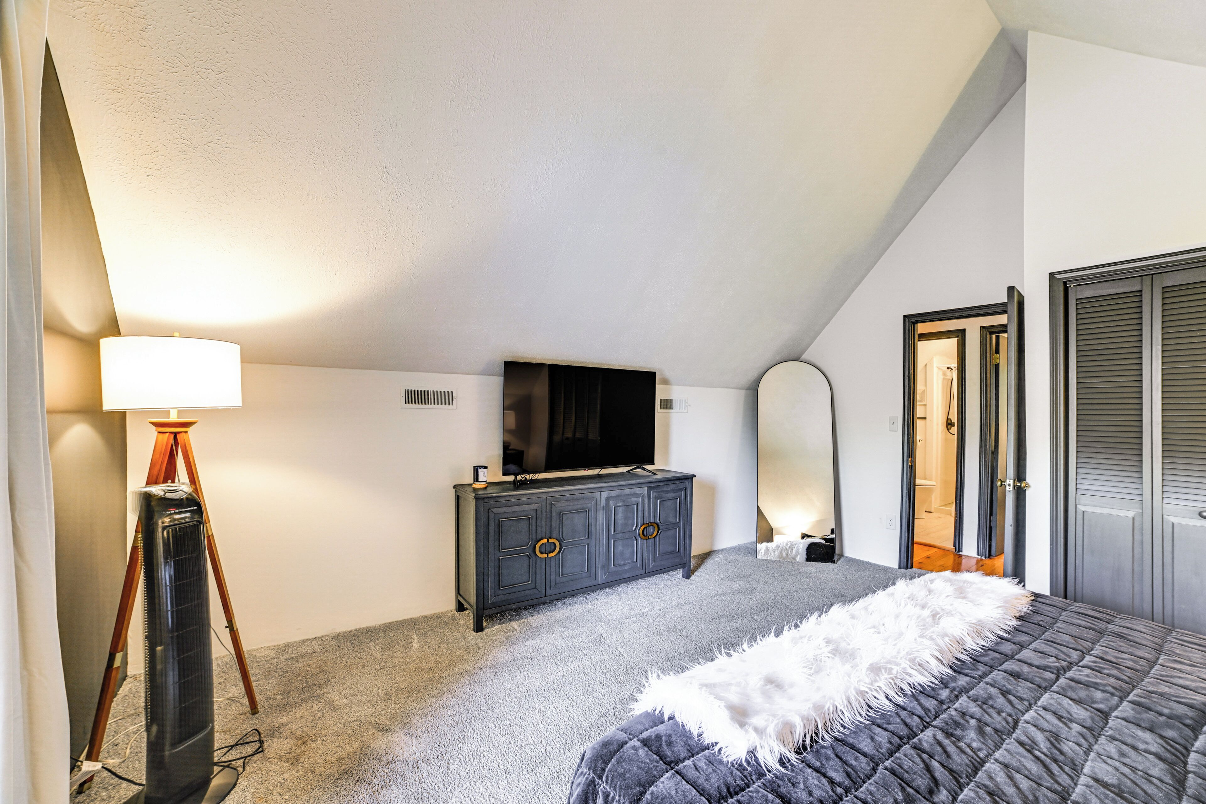 A bedroom with a bed, a dresser, a TV, and a mirror.