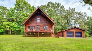A log cabin with a porch, a garage, and a grassy yard.