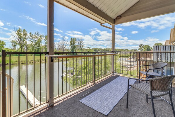 A covered balcony with a view of a river, a dock, and outdoor furniture.
