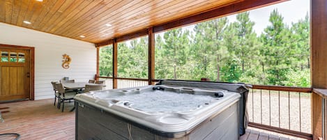 A wooden deck with a hot tub, outdoor seating, and a view of trees.