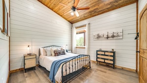 Une chambre à coucher avec un lit, un plancher en bois, un ventilateur de plafond, une table de chevet et une commode.