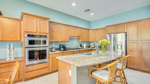 A modern kitchen with wooden cabinets, stainless steel appliances, a granite countertop, and wicker bar stools. - Spacious Home in Saddlebrooke 55-plus Community! (Saddlebrooke)
