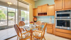 A kitchen with wooden cabinets, a stainless steel oven, and a dining area with wicker chairs and a glass table. - Spacious Home in Saddlebrooke 55-plus Community! (Saddlebrooke)