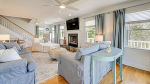 A spacious living room with a staircase, a fireplace, and a large window with curtains.