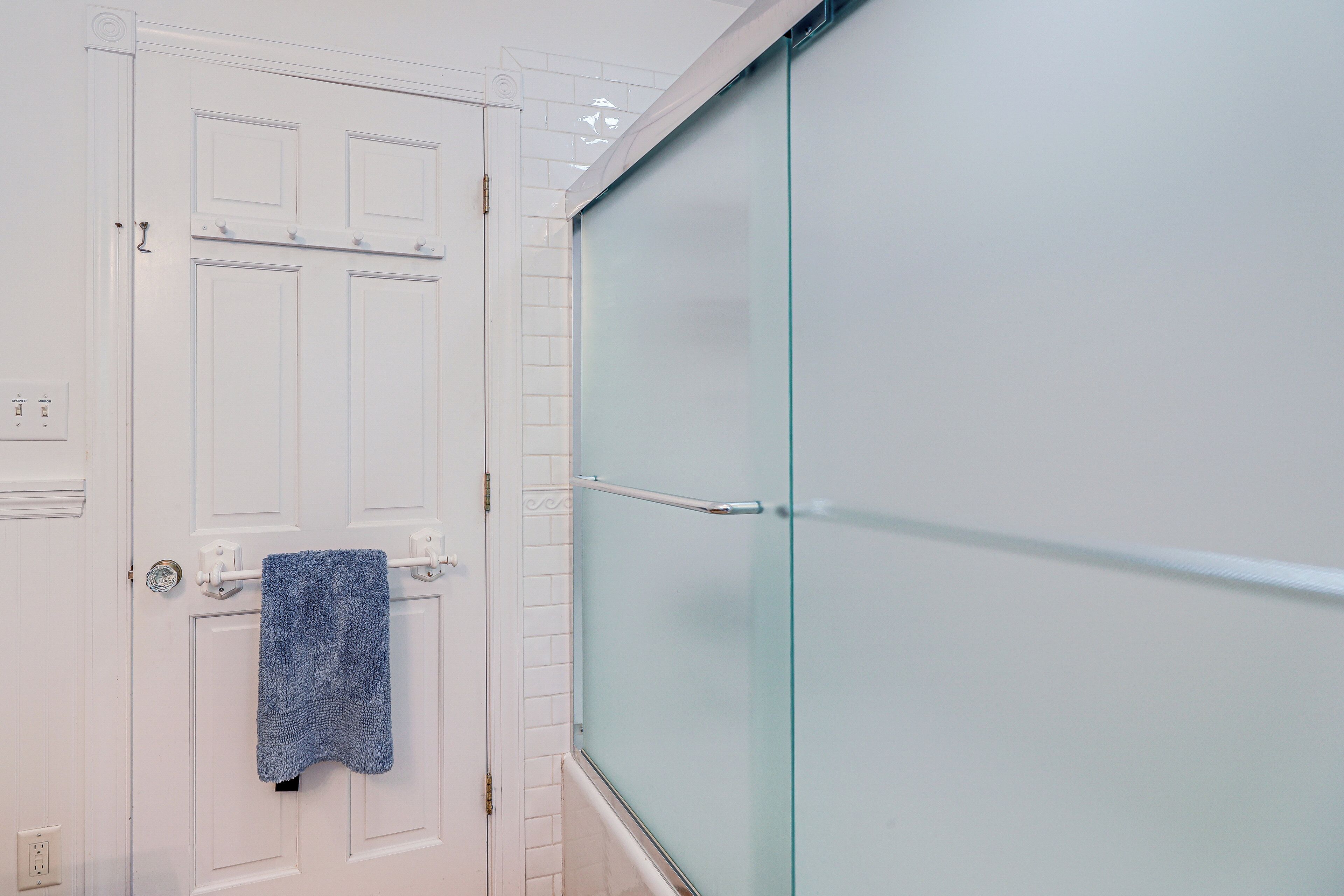 A bathroom with a white door, a towel hanging on a towel rack, and a glass shower enclosure.