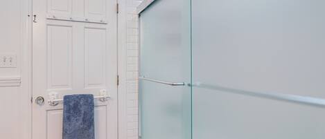 A bathroom with a white door, a towel hanging on a towel rack, and a glass shower enclosure.