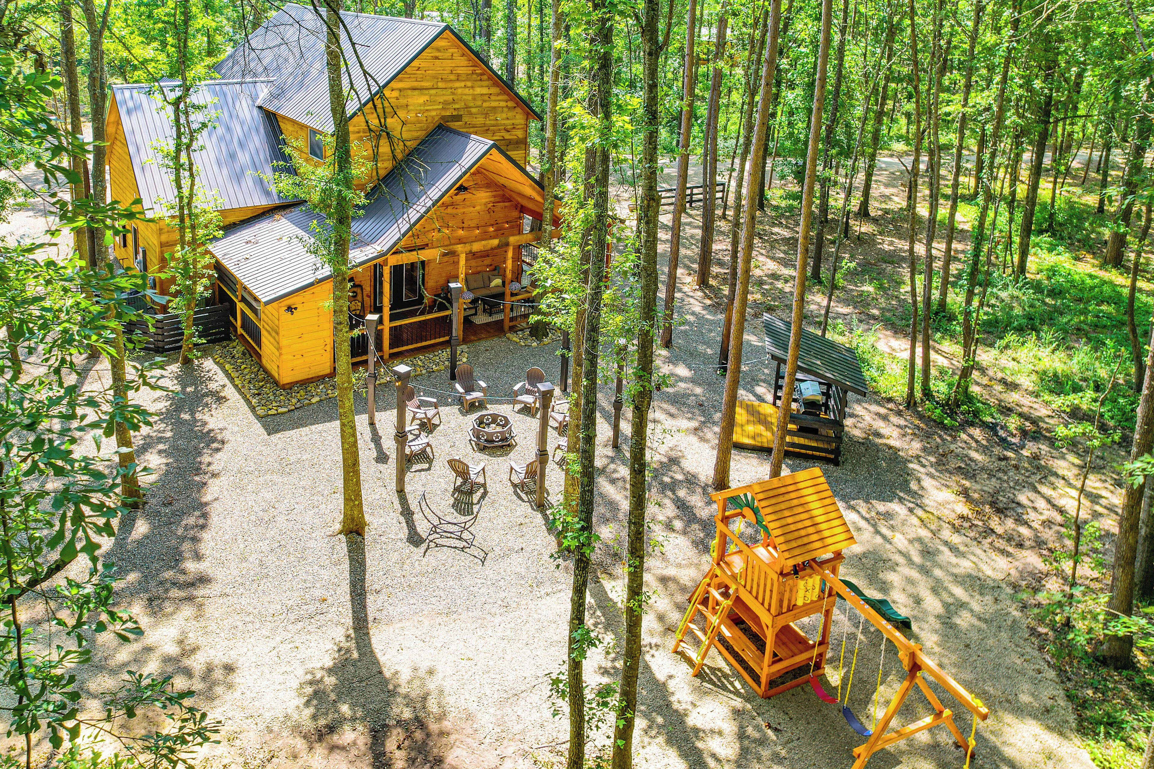 A wooden cabin with a deck and outdoor seating area surrounded by trees.