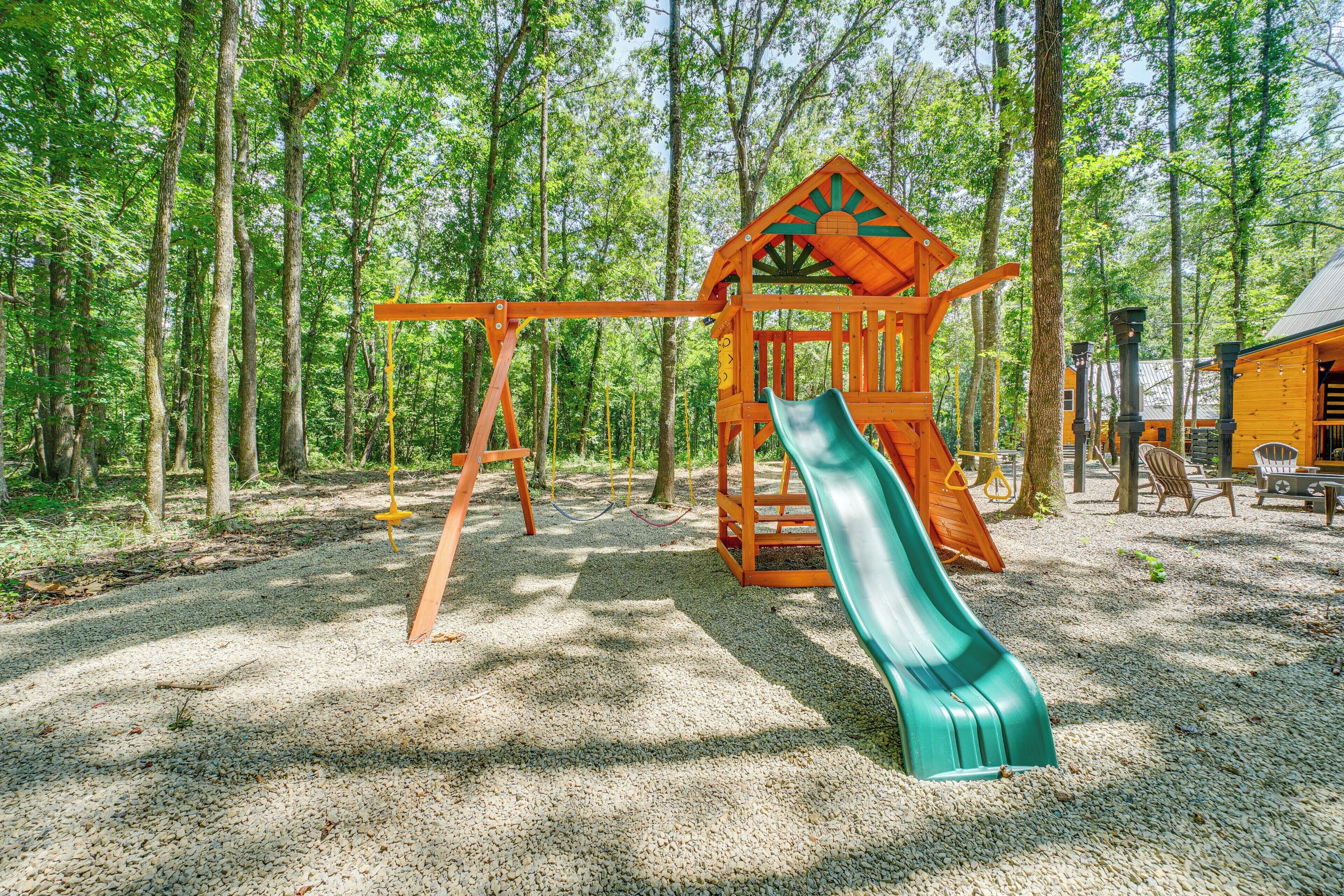 A playground with a slide and swings set in a forested area.
