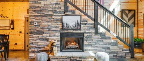 A stone fireplace with a framed picture above it, a wooden staircase with a metal railing, and a wooden floor.