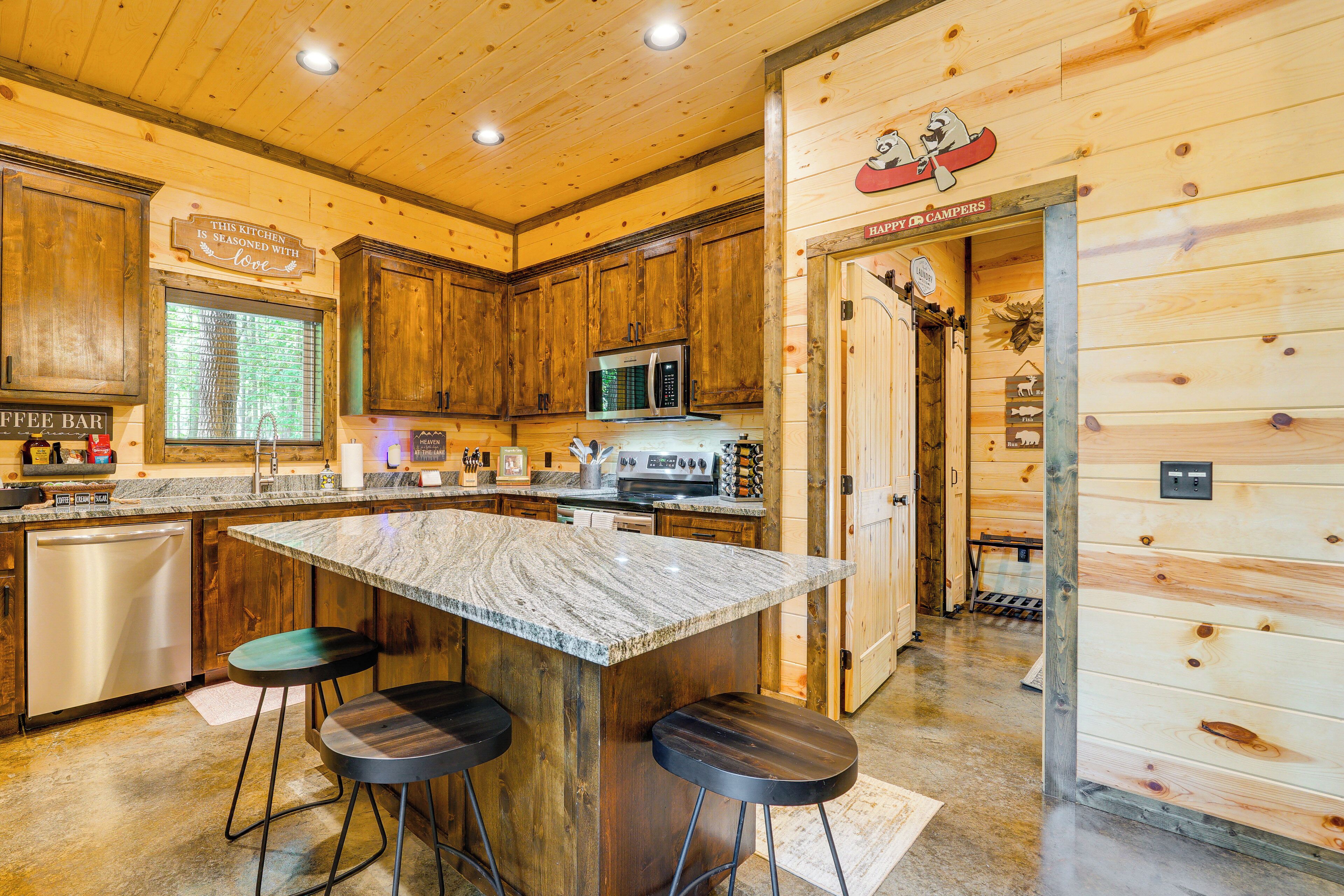 Una cocina con armarios de madera, encimera de granito, una barra de café y un cartel que dice 'This kitchen is seasoned with love'.